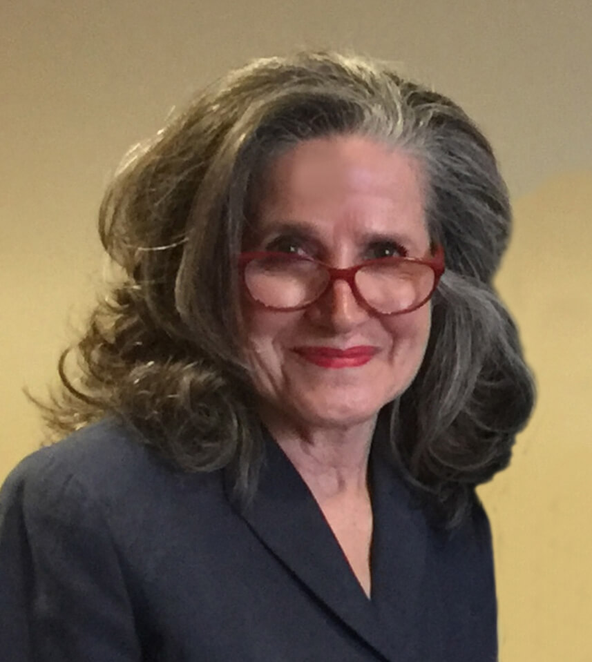 A woman in a suit and glasses is smiling.